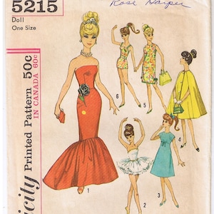 May include: A vintage Simplicity sewing pattern for a doll, featuring six different outfits. The pattern number is 5215 and the price is 50 cents. The outfits include a red gown, a white tutu, a blue dress, a yellow cape, and two other dresses.