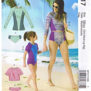 May include: McCall's M7417 sewing pattern featuring swimwear designs. The pattern includes options for a long-sleeved top, high-waisted bottoms, and a short-sleeved rash guard. The swimwear designs feature various patterns and color combinations, including purple, blue, and patterned fabrics.