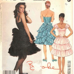 May include: McCall's sewing pattern featuring three dress designs. The dresses include a black strapless dress with a ruffled skirt, a blue strapless dress with a large bow, and a pink polka-dot dress with cap sleeves. The pattern number is 3349.