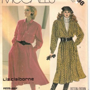 May include: Vintage McCall's sewing pattern featuring two Liz Claiborne dress designs. One dress is a long-sleeved, button-down style in a reddish-pink hue, cinched at the waist with a black belt. The other is a yellow and black plaid coat dress with a black belt.