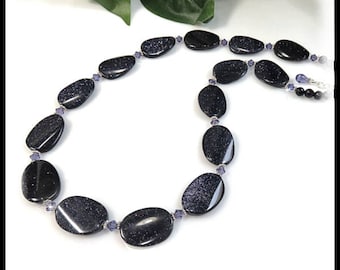 Puede incluir: Un collar hecho de piedras ovaladas de color azul oscuro con detalles plateados y pequeñas cuentas moradas.