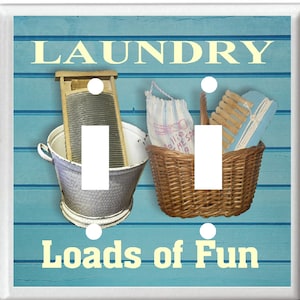May include: A light blue double light switch cover with the text "Laundry Loads of Fun" in yellow. The switch cover features a vintage washboard, a basket of clothes, and a blue and white laundry bag.