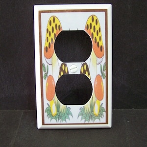 May include: White ceramic light switch cover with a brown border. The cover features a design of two yellow and orange mushrooms with brown spots on a white background.