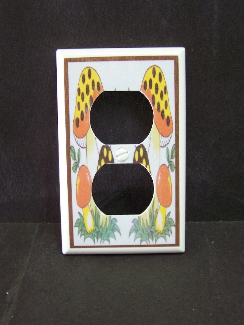 May include: White ceramic light switch cover with a brown border. The cover features a design of two yellow and orange mushrooms with brown spots on a white background.