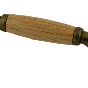 May include: A brass cabinet pull with a wooden handle. The handle is a light brown color and has a slightly rounded shape. The brass is a dark, antique finish.