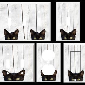 May include: A set of six light switch and outlet covers featuring a black cat peeking out from behind white painted wood planks. The cat's eyes are bright yellow.