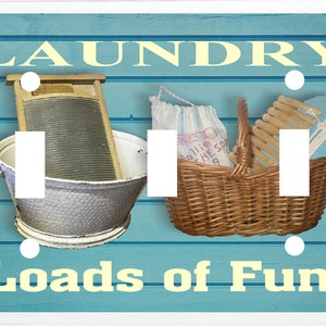 May include: A light blue wooden light switch cover with a vintage laundry theme. The cover features a washboard, a basket of clothes, and the text "Laundry Loads of Fun".