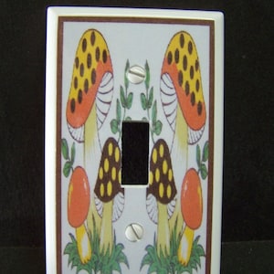 May include: White light switch cover with a brown border and a colorful mushroom design. The mushrooms are red, yellow, brown, and white with black spots.