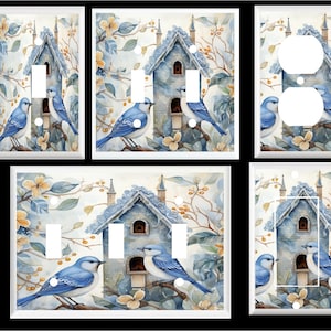 May include: A set of light switch and outlet covers featuring a watercolor painting of a bluebird perched on a birdhouse with a white roof and blue trim. The birdhouse is surrounded by green leaves and yellow flowers.