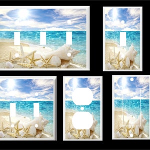 May include: A set of five white light switch and outlet covers featuring a beach scene with blue water, white sand, seashells, and starfish. The covers are designed to add a coastal touch to any room.