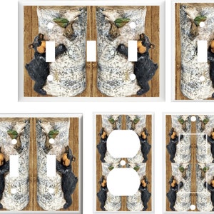May include: A set of light switch and outlet covers featuring a black bear climbing a birch tree with a green leaf on a brown wood background.
