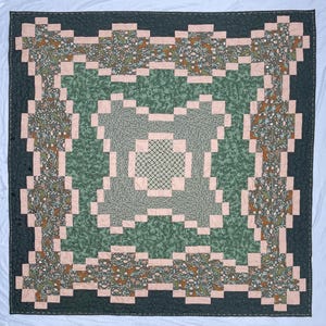 Puede incluir: Una colcha de patchwork cuadrada que presenta un bloque central de patrones geométricos blancos y verdes rodeado de tela de follaje verde salvia. El diseño incluye un borde de cuadrícula rosa claro y paneles exteriores de tela verde oscuro con motivos florales.