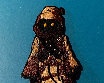 May include: Embroidered patch of a brown robed figure with yellow eyes. The figure is standing with its arms crossed.