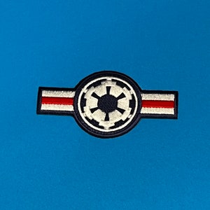 May include: A black and white embroidered patch with the Imperial symbol from Star Wars. The patch has a red and white stripe across the top.