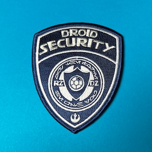 May include: A blue and white embroidered patch with the text "Droid Security" and a logo featuring the text "R2-D2" and "C-3PO".