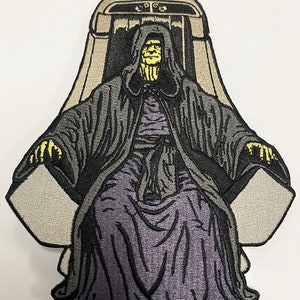 May include: An embroidered patch featuring a dark-robed figure with a yellow face sitting on a throne. The figure has a hood and is holding their hands in a gesture of power. The throne is decorated with intricate details.