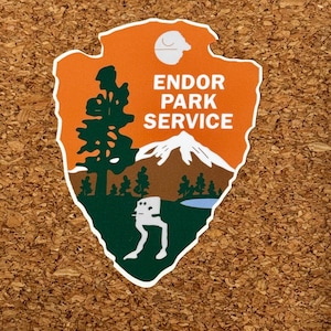 Pode incluir: Um autocolante recortado com um design laranja e verde. O autocolante apresenta uma montanha, árvores e um walker AT-ST branco. O texto "ENDOR PARK SERVICE" é branco. Uma Estrela da Morte branca está no canto superior direito.