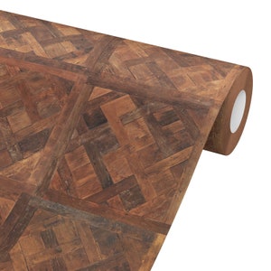 May include: A roll of brown wood-look wallpaper with a parquet pattern. The design features a repeating geometric arrangement of rectangular and square wooden pieces in varying shades of brown, creating a textured appearance.