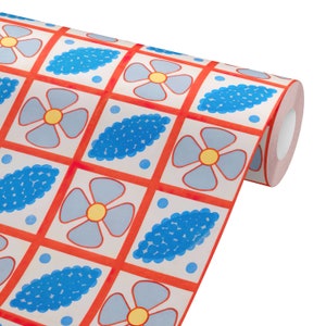 May include: Roll of patterned wallpaper featuring a repeating design of blue flowers and blue oval shapes within red squares. The flowers have yellow centers. The wallpaper is on a white background.