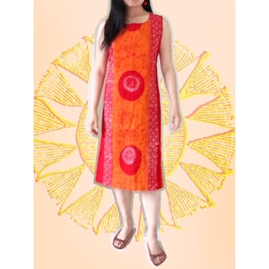 May include: Sleeveless orange and red dress with a round neckline. The dress features a central panel with two red circular designs and red side panels with a white floral pattern. The dress is knee-length and worn with brown sandals.