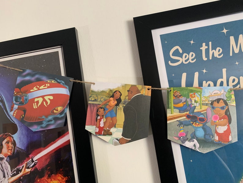 May include: A string of colorful paper pennants with images from Disney movies, including Lilo & Stitch, Moana, and Stitch. The pennants are strung together with twine and are hanging on a wall.