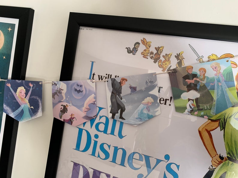 May include: A Frozen themed banner with images of Elsa, Olaf, Anna, and Kristoff. The banner is strung with white twine and has a blue and white color scheme. The banner says "It will..." and "Walt Disney's Frozen".