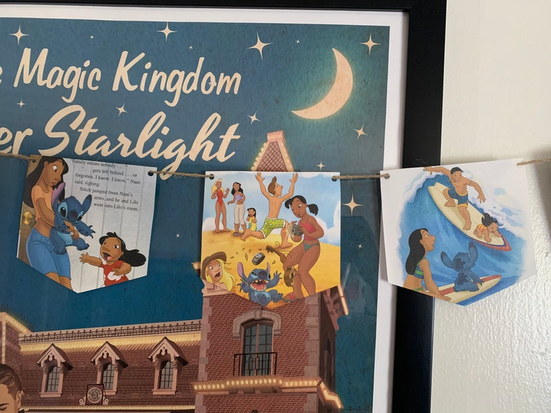 May include: A blue and white banner with a string of flags featuring characters from the Disney movie Lilo & Stitch. The flags feature Stitch, Lilo, and other characters from the movie. The banner is hanging on a wall with a framed poster behind it. The poster features the text "Magic Kingdom Under Starlight".