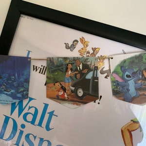 May include: A string of colorful fabric pennants with Disney characters from the movies Lilo & Stitch, The Princess and the Frog, and The Lion King. The pennants are strung together with twine and are hanging from a wall.
