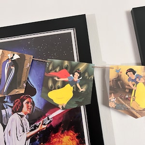 May include: A string of colorful banners featuring characters from the Disney movie Snow White and the Seven Dwarfs. The banners are hung on a wall with a black frame and a Star Wars poster.