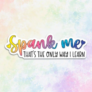 May include: A sticker with a rainbow gradient design that says "Spank me that's the only way I learn".