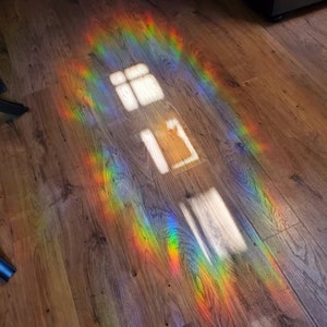 May include: A wooden floor is illuminated by a vibrant rainbow spectrum of light. The light creates a colorful pattern, with bright hues of red, orange, yellow, green, blue, and purple. The image also shows the reflection of a window.