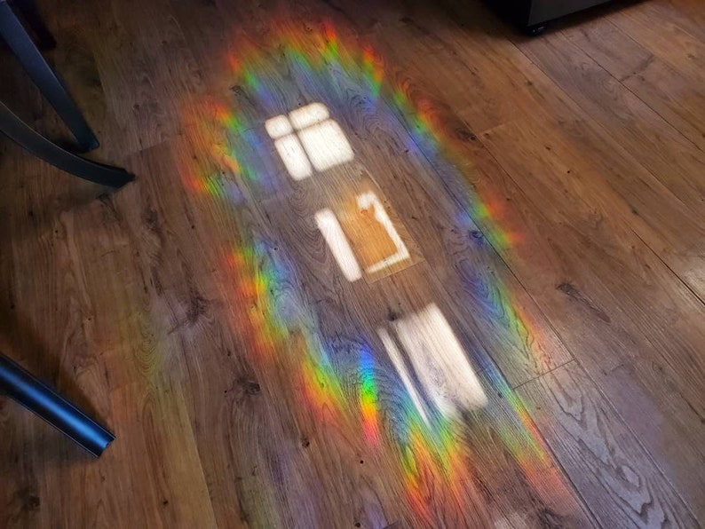 May include: A wooden floor is illuminated by a vibrant rainbow spectrum of light. The light creates a colorful pattern, with bright hues of red, orange, yellow, green, blue, and purple. The image also shows the reflection of a window.