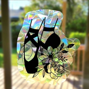 May include: A holographic sticker featuring a black silhouette of ballet pointe shoes and a floral arrangement. The sticker has a shimmering, iridescent finish, with a design of a pair of ballet shoes and a bouquet of flowers.