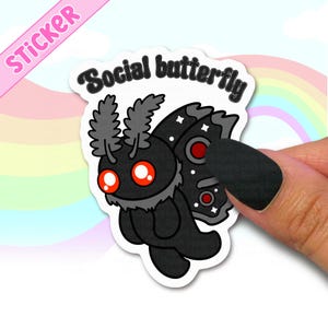 May include: A sticker featuring a cartoon moth with a black body, gray accents, and red eyes. The sticker has the text "Social butterfly" in black, and the word "STICKER" in pink. The background is a rainbow.