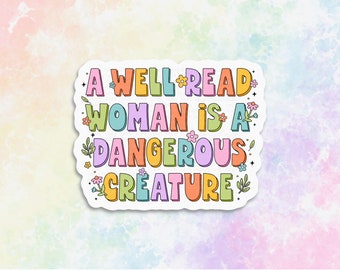 May include: A colorful sticker with the text "A WELL READ WOMAN IS A DANGEROUS CREATURE" in bubble letters. The sticker has a white border and is decorated with small flowers and leaves. The background is a pastel watercolor wash.