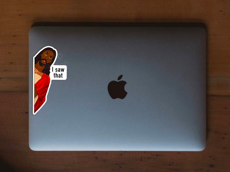 Pode incluir: Um adesivo de uma pessoa com pele escura e cabelo comprido vestindo uma t&uacute;nica vermelha e olhando por cima do ombro. O adesivo est&aacute; em um laptop prateado com um logotipo da Apple preto. O adesivo diz "Eu vi isso".