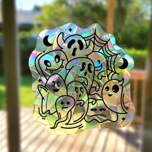 May include: A holographic sticker featuring a group of cartoon ghosts with different expressions and poses. The ghosts are surrounded by a web and stars.