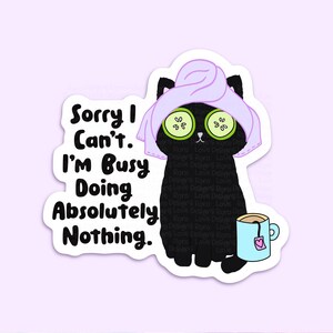 Puede incluir: Un gato negro con una toalla morada en la cabeza y rodajas de pepino sobre los ojos, sosteniendo una taza de t&eacute; azul con un coraz&oacute;n rosa. El texto "Sorry I Can't. I'm Busy Doing Absolutely Nothing." est&aacute; escrito en negro sobre un fondo blanco.