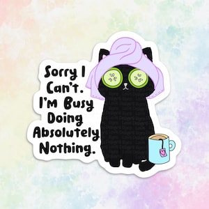 Puede incluir: Un gato negro con una toalla morada en la cabeza y rodajas de pepino sobre los ojos, sosteniendo una taza de t&eacute; azul con una bolsita de t&eacute; de coraz&oacute;n rosa. El texto "Sorry I Can't. I'm Busy Doing Absolutely Nothing." est&aacute; escrito en negro sobre un fondo blanco.