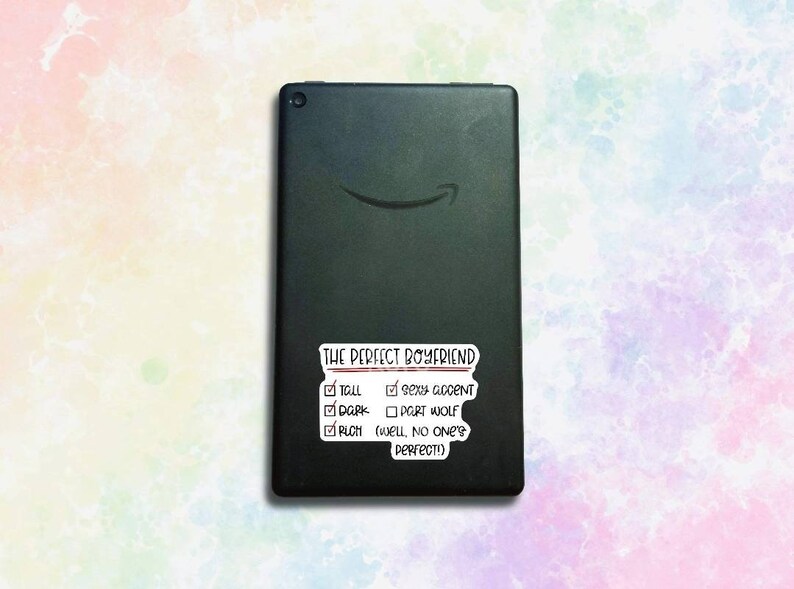 May include: A black tablet with a white sticker that says "THE PERFECT BOYFRIEND" with a checklist of qualities. The checklist includes "Tall", "Sexy Accent", "Dark", "Port Wolf", and "Rich (Well, no one's perfect!)"