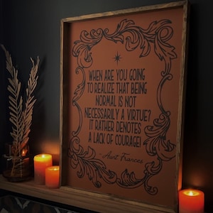 Op de afbeelding: Een ingelijst print met een bruine achtergrond en zwarte tekst. De tekst luidt "Wanneer ga je beseffen dat normaal zijn geen deugd is? Het duidt eerder op een gebrek aan moed! - Tante Frances".