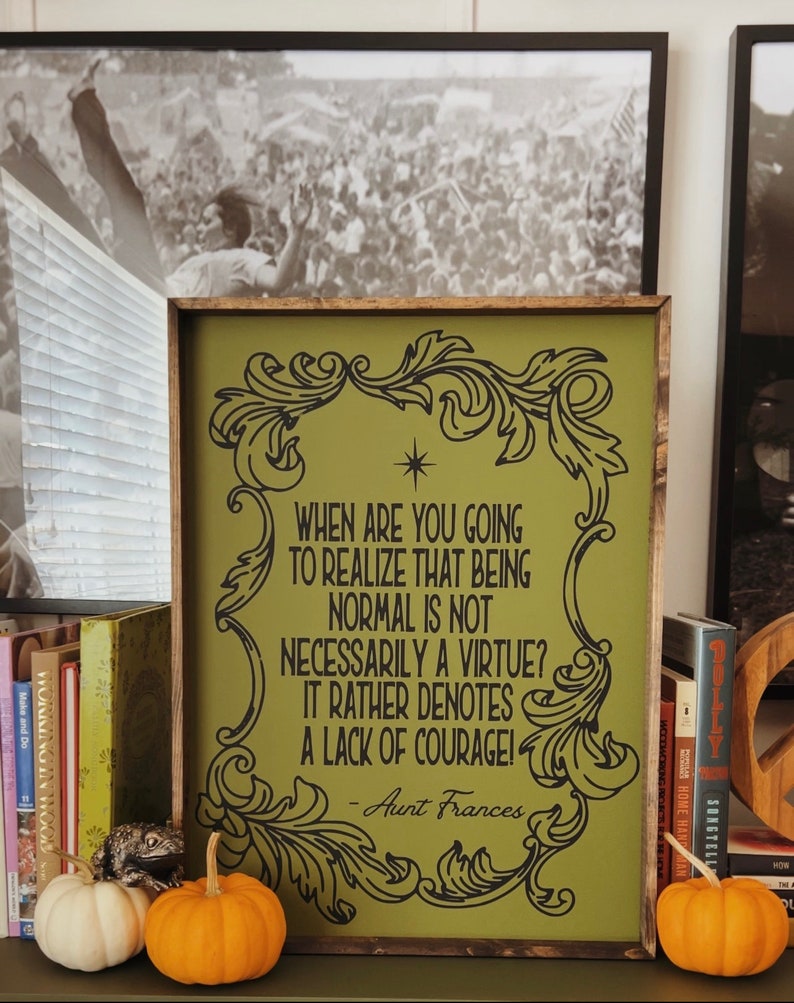 Op de afbeelding: Een groen houten bord met een zwart, versierd frame en een citaat dat luidt: "Wanneer ga je beseffen dat normaal zijn niet per se een deugd is? Het duidt eerder op een gebrek aan moed! - Tante Frances"