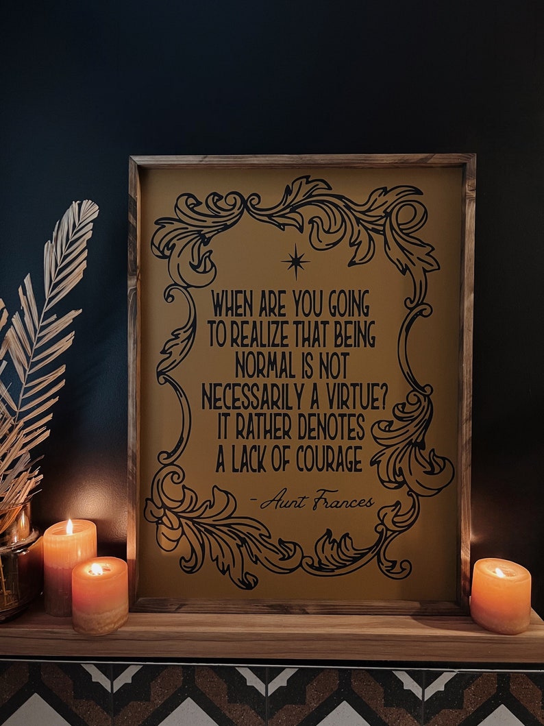 Op de afbeelding: Een ingelijst print met een gouden achtergrond en zwarte tekst. De tekst luidt: "Wanneer ga je beseffen dat normaal zijn niet per se een deugd is? Het duidt eerder op een gebrek aan moed - Tante Frances".