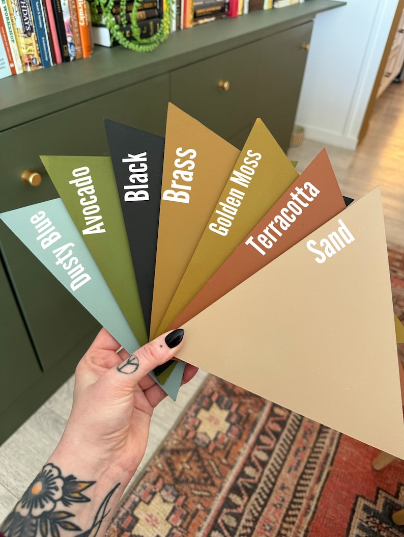 Op de afbeelding: Een waaier met acht verfstalen. De kleuren zijn Stofblauw, Avocado, Zwart, Messing, Gouden Mos, Terracotta, Zand en een donkergroen.
