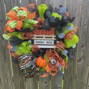 Op de afbeelding: Een Halloween-krans met oranje, groene en zwarte mesh, linten en decoratieve elementen. Voorzien van een bord met de tekst "PUMPKIN PATCH" en een kleine pompoen. Bevat tekst met de tekst "Beware! Scary" en "Happy Halloween Boo!"