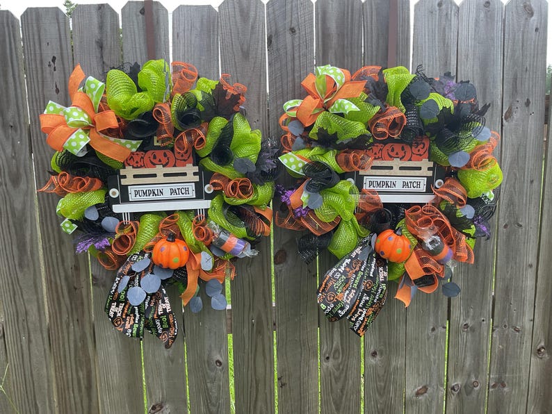 Op de afbeelding: Twee Halloween-kransen met groene, oranje en zwarte mesh, linten en decoratieve elementen. Elke krans heeft een bord met de tekst "Pumpkin Patch", een kleine oranje pompoen en een decoratieve tas. De kransen hangen aan een houten hek.