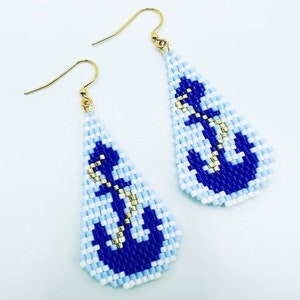 May include: A pair of beaded earrings with a nautical theme. The earrings are teardrop-shaped, featuring a blue anchor design on a light blue and white background. Gold-coloured hooks complete the design.