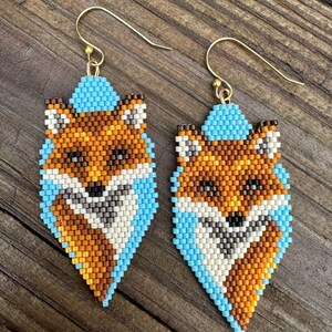 Puede incluir: Un par de pendientes de cuentas con dise&ntilde;o de zorro. Los pendientes presentan un dise&ntilde;o de zorro con cuentas naranjas, blancas, marrones y azul claro. Los pendientes tienen ganchos dorados.