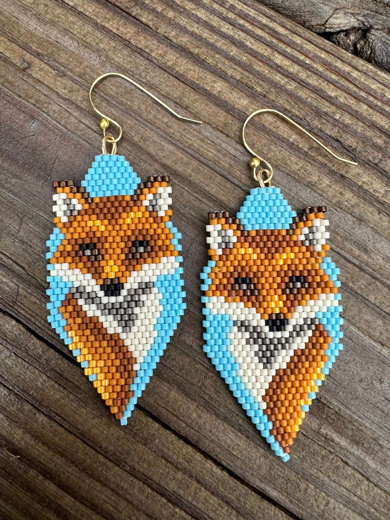 Puede incluir: Un par de pendientes de cuentas con dise&ntilde;o de zorro. Los pendientes presentan un dise&ntilde;o de zorro con cuentas naranjas, blancas, marrones y azul claro. Los pendientes tienen ganchos dorados.