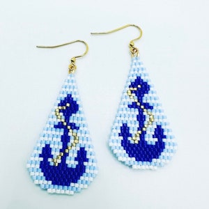 May include: A pair of teardrop earrings with a nautical theme. The earrings feature a beaded design with a blue anchor on a light blue and white background. Gold-coloured hooks complete the design.